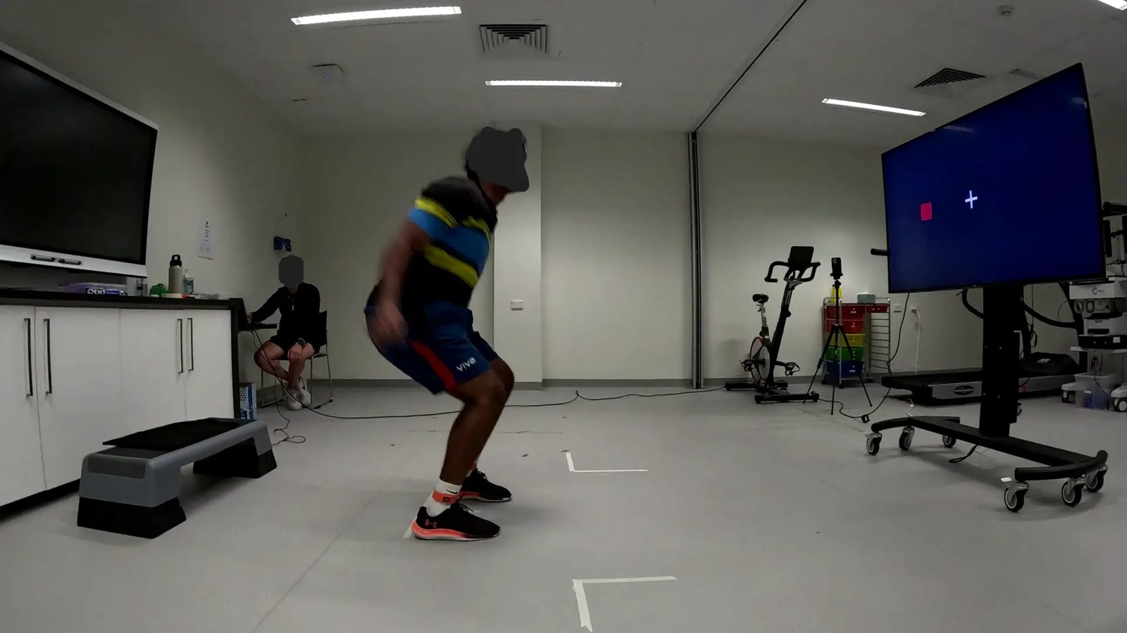 Athlete mid-flight after leaving the box, with a red directional cue showing on the lab display.